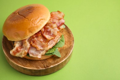 Photo of Delicious burger with bacon and greens on green table, closeup. Space for text