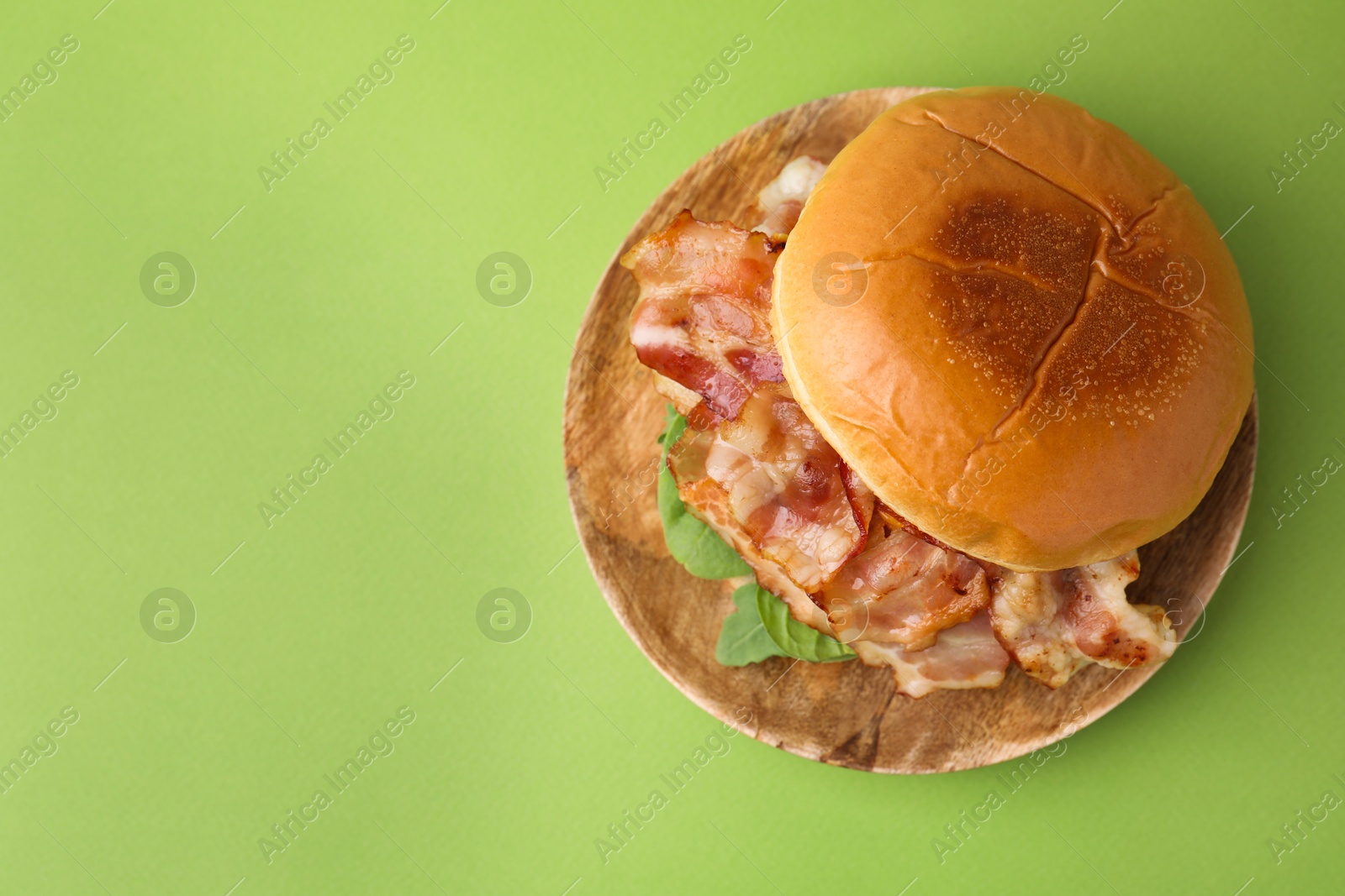 Photo of Delicious burger with bacon and greens on green table, top view. Space for text