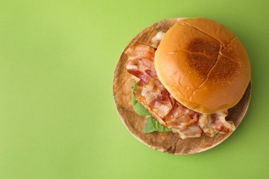 Delicious burger with bacon and greens on green table, top view. Space for text