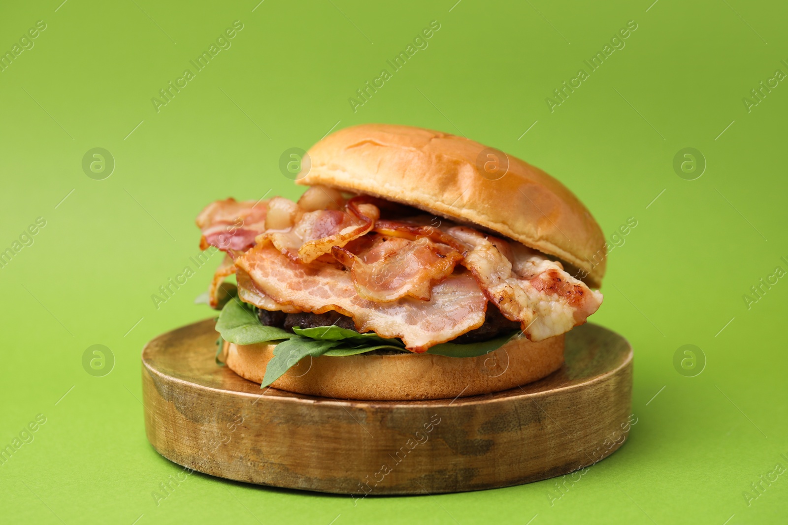 Photo of Delicious burger with bacon and greens on green background, closeup