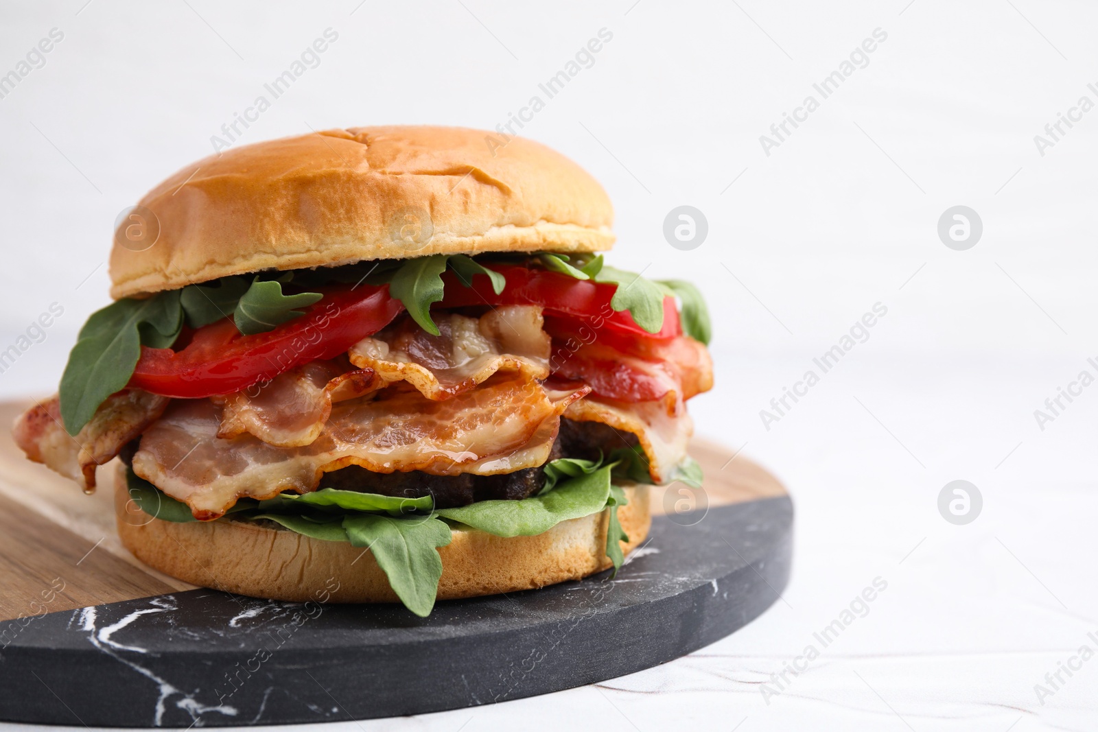 Photo of Delicious burger with bacon, tomato and greens on light background, closeup. Space for text