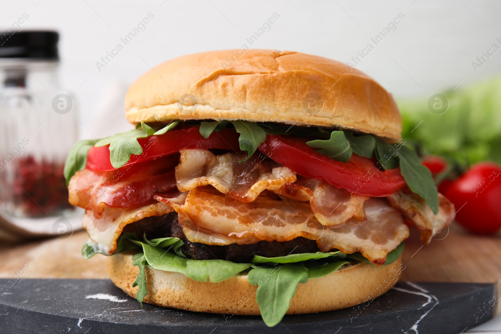 Photo of Delicious burger with bacon, tomato and greens on table, closeup