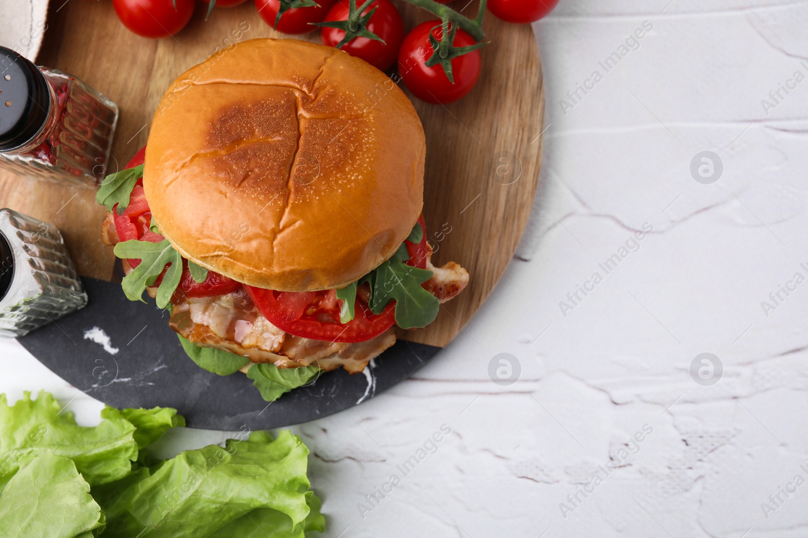 Photo of Delicious burger with bacon, tomatoes and lettuce on light textured table, flat lay. Space for text