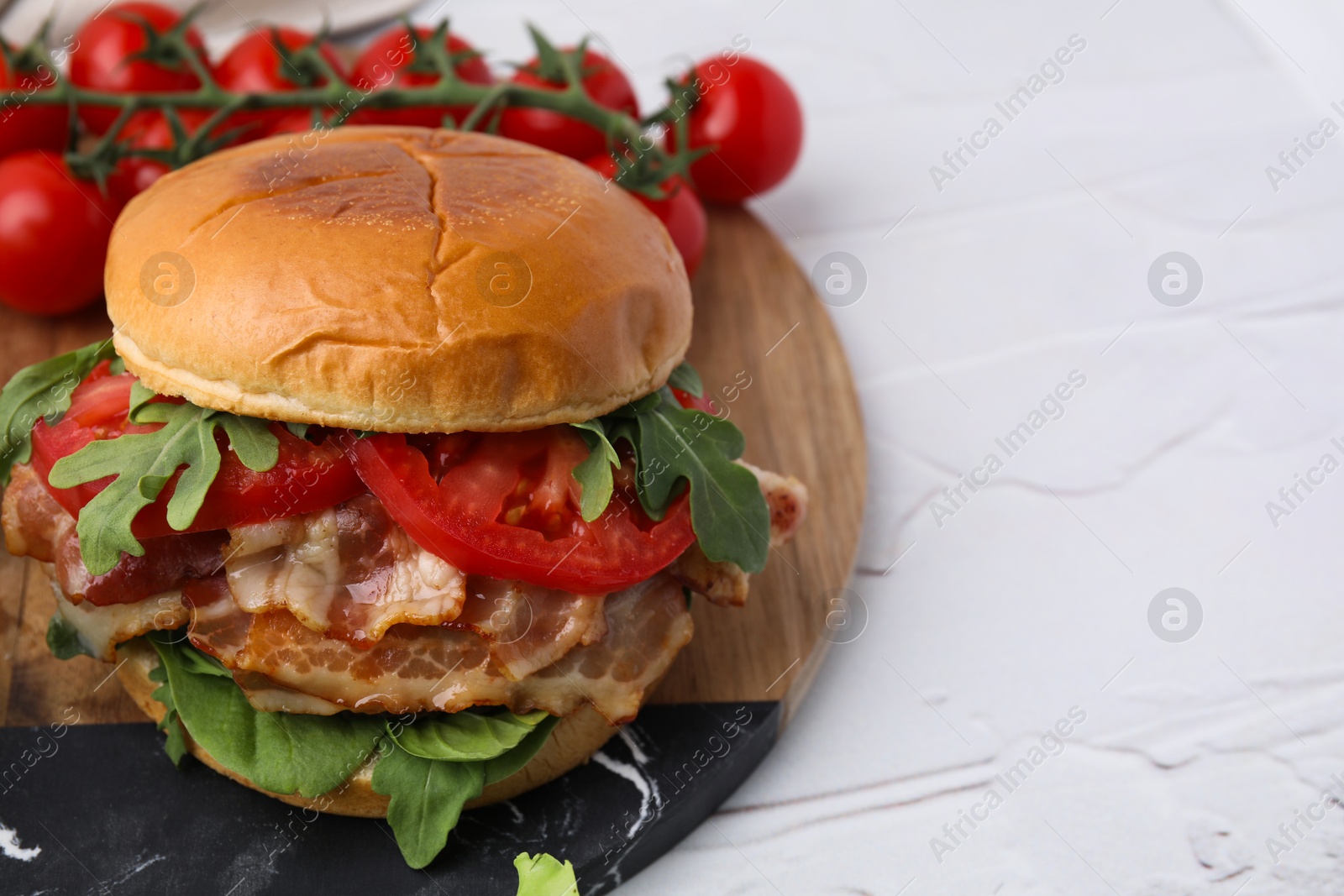 Photo of Delicious burger with bacon, tomato and greens on light textured table, closeup. Space for text