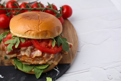 Delicious burger with bacon, tomato and greens on light textured table, closeup. Space for text