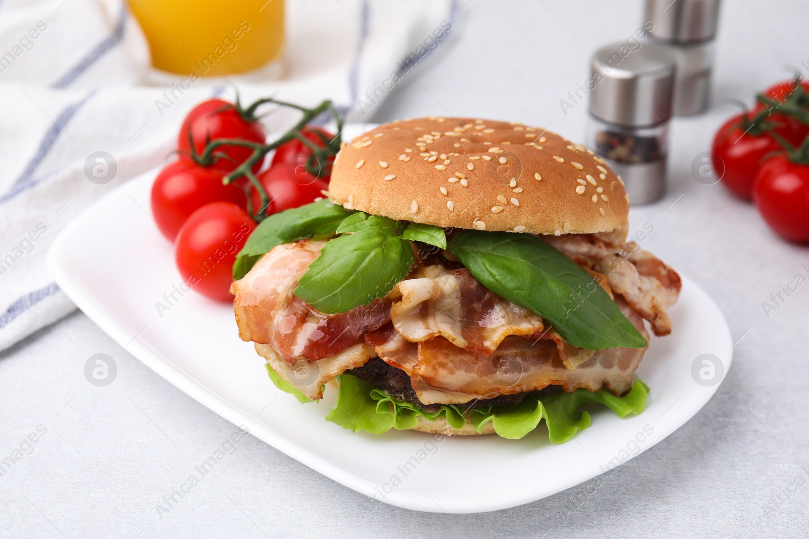 Photo of Delicious burger with bacon, greens and tomatoes on light table