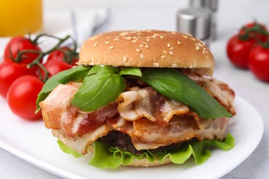 Photo of Delicious burger with bacon, greens and tomatoes on light table, closeup