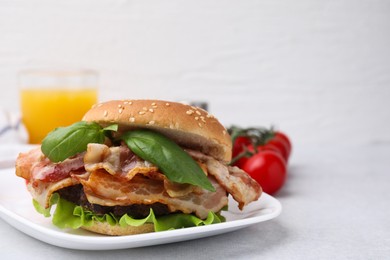 Photo of Delicious burger with bacon and greens on light table, closeup. Space for text