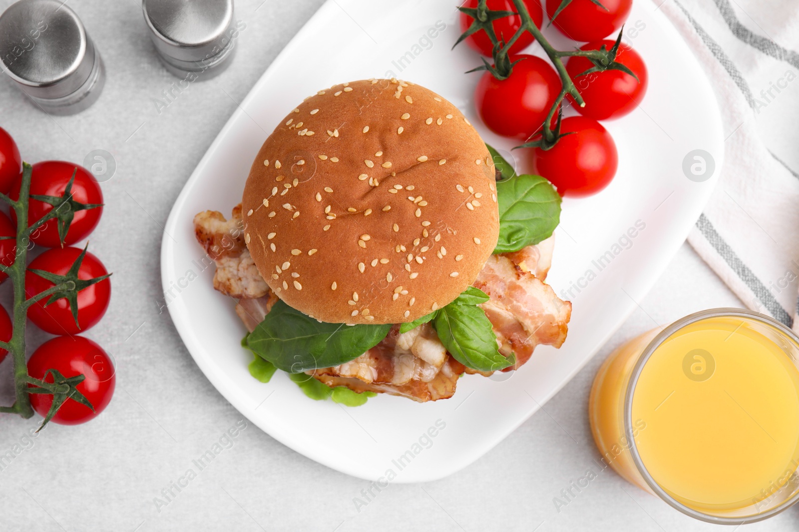 Photo of Delicious burger with bacon, greens, tomatoes and juice on light table, flat lay