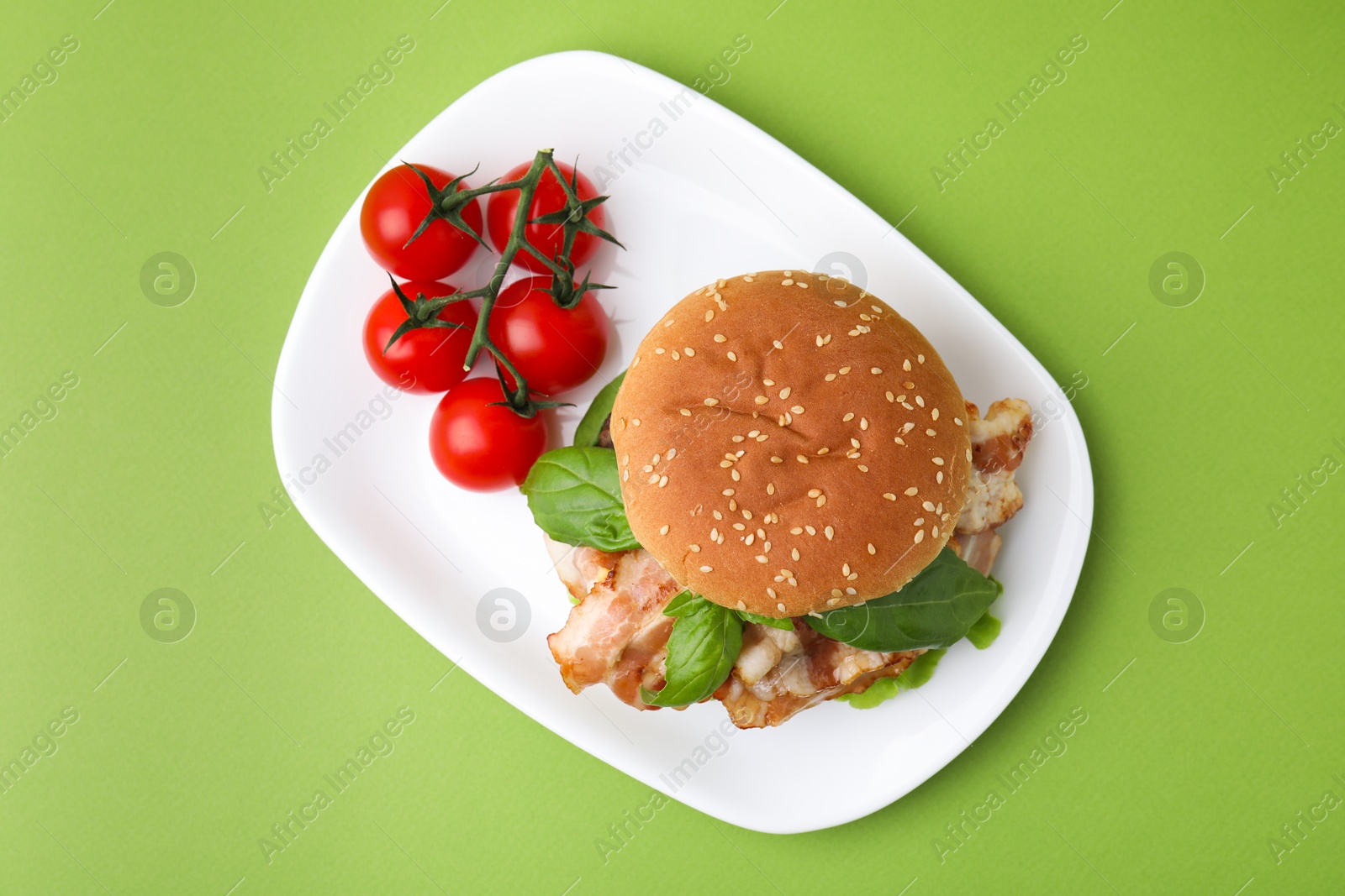 Photo of Delicious burger with bacon, basil and tomatoes green table, top view