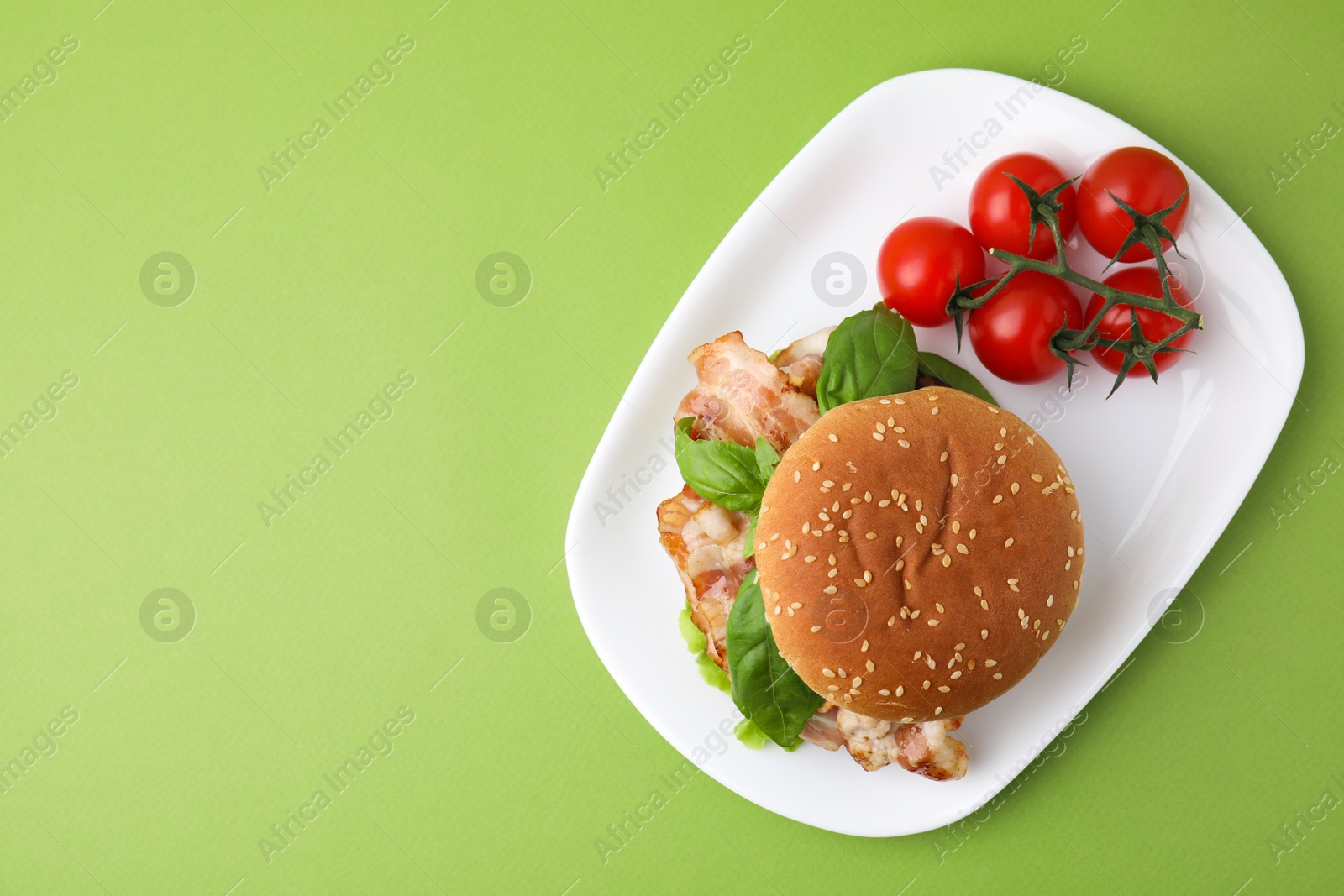 Photo of Delicious burger with bacon, basil and tomatoes green table, top view. Space for text