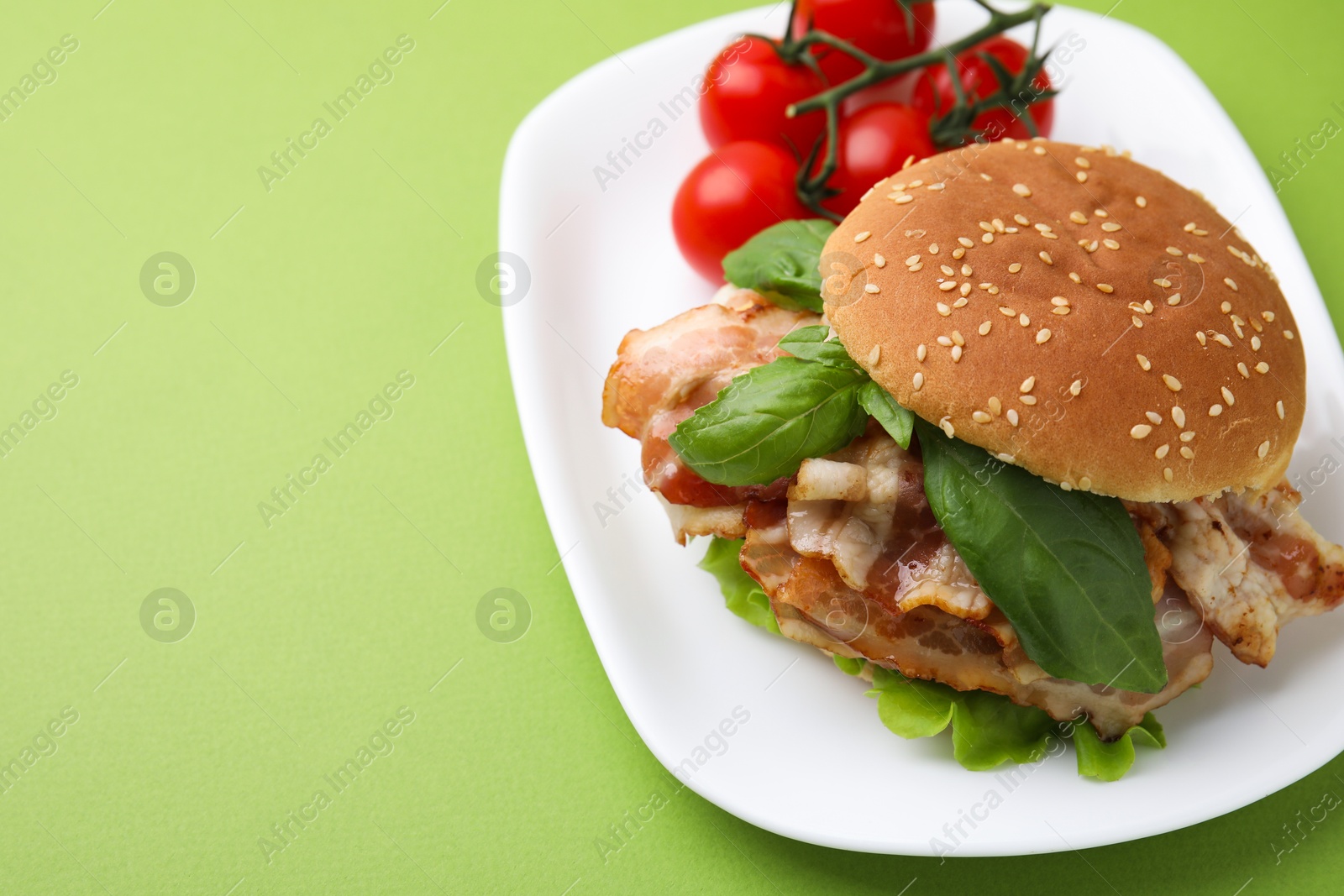 Photo of Delicious burger with bacon, basil and tomatoes green table. Space for text