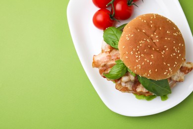 Delicious burger with bacon, basil and tomatoes green table, top view. Space for text