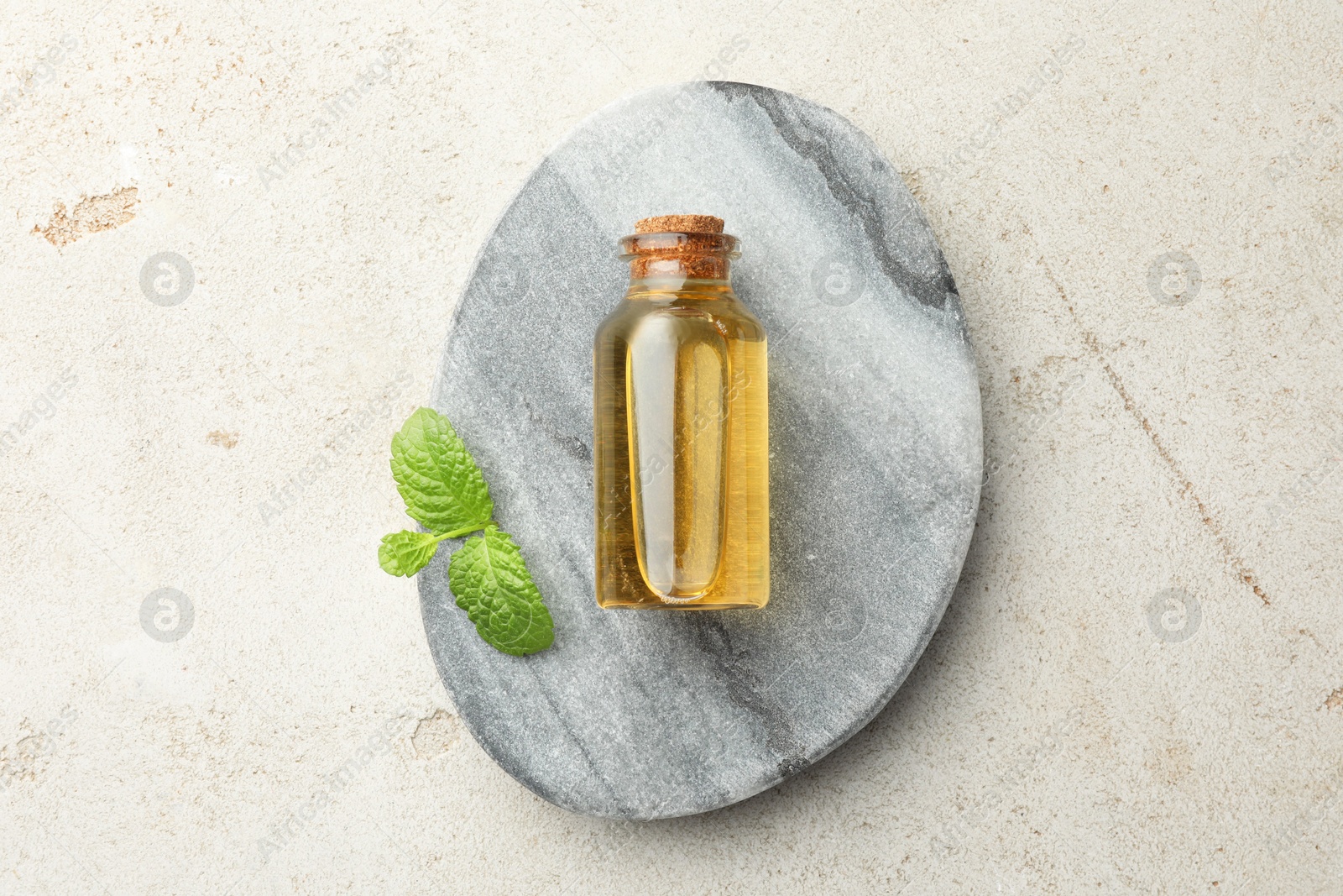 Photo of Bottle of essential oil and mint on light textured table, top view