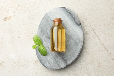 Photo of Bottle of essential oil and mint on light textured table, top view