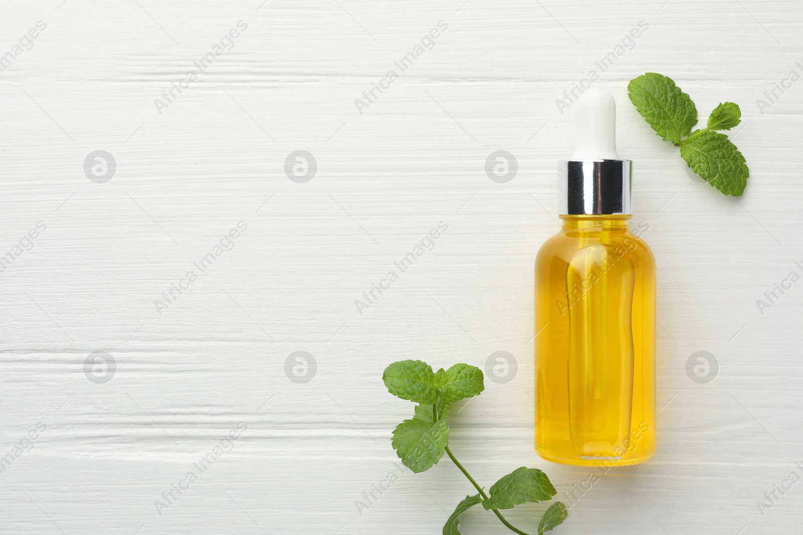 Photo of Bottle of essential oil and mint on white wooden table, flat lay. Space for text