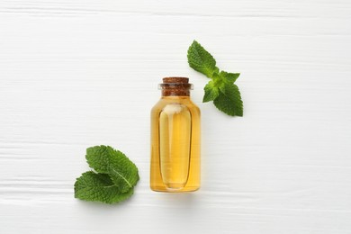 Photo of Bottle of essential oil and mint on white wooden table, flat lay