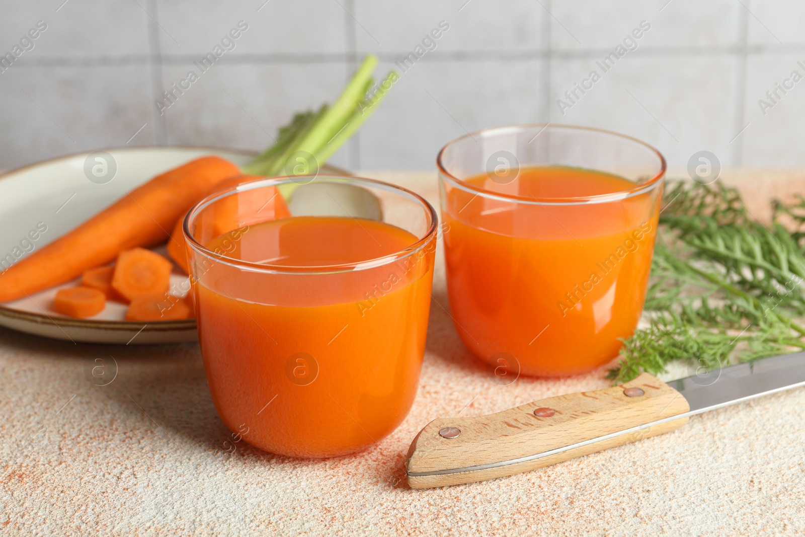 Photo of Healthy carrot juice in glasses, fresh vegetables and knife on color textured table