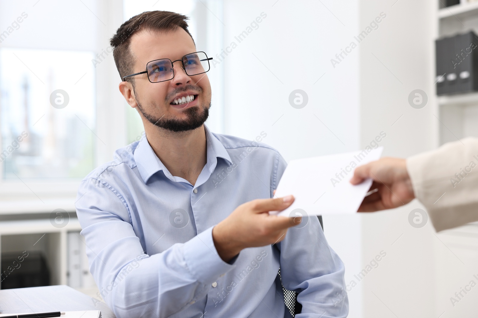 Photo of Smiling employee receiving envelope with salary from boss in office