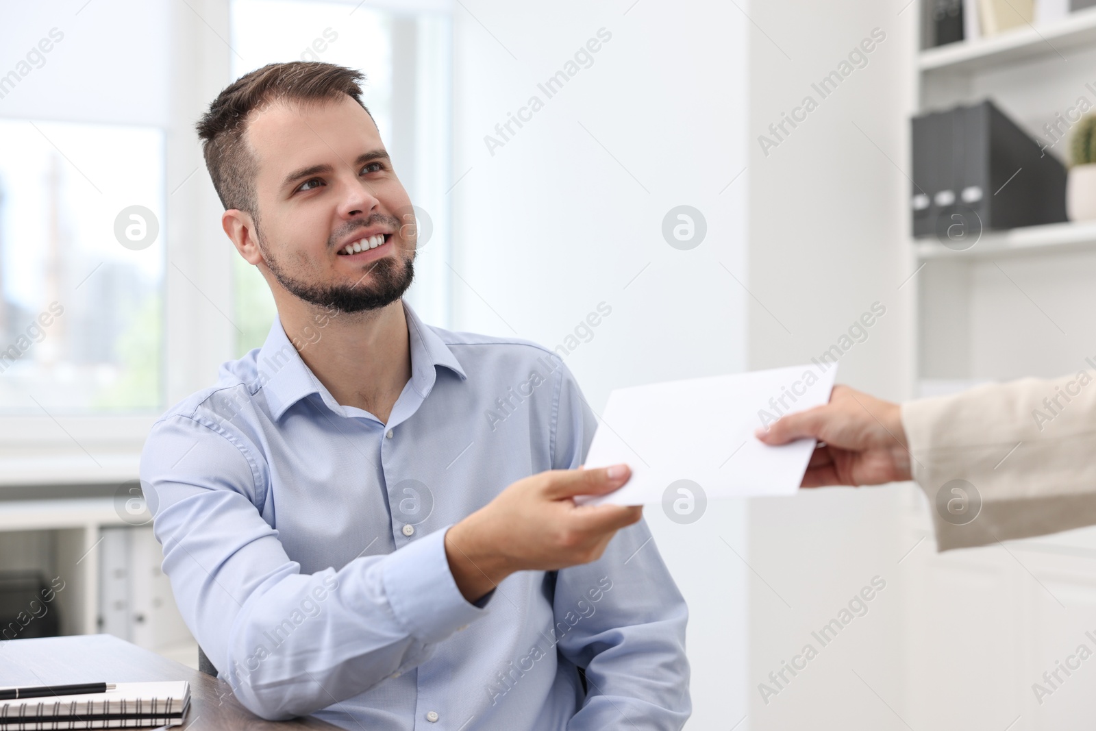 Photo of Smiling employee receiving envelope with salary from boss in office