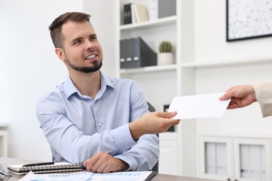 Photo of Smiling employee receiving envelope with salary from boss in office