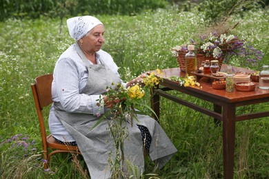 Senior woman with different ingredients for tincture at wooden table outdoors