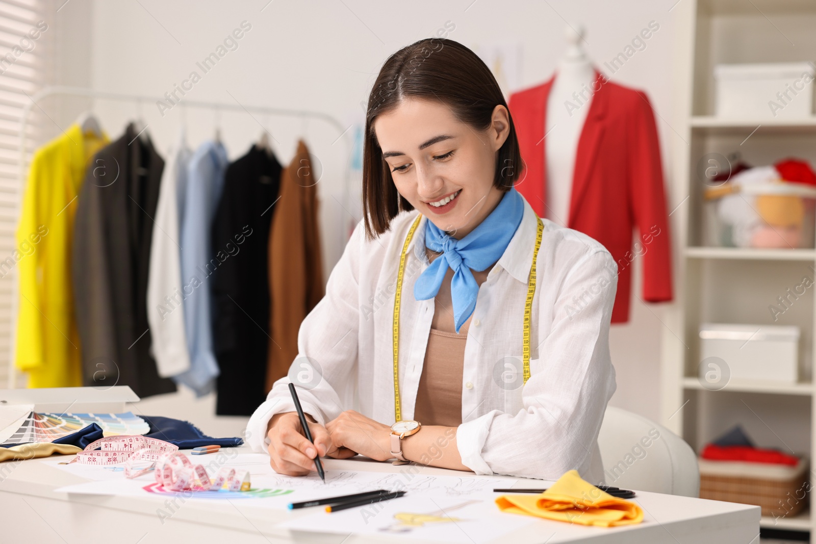 Photo of Fashion designer drawing sketch of beautiful outfit at table in workshop