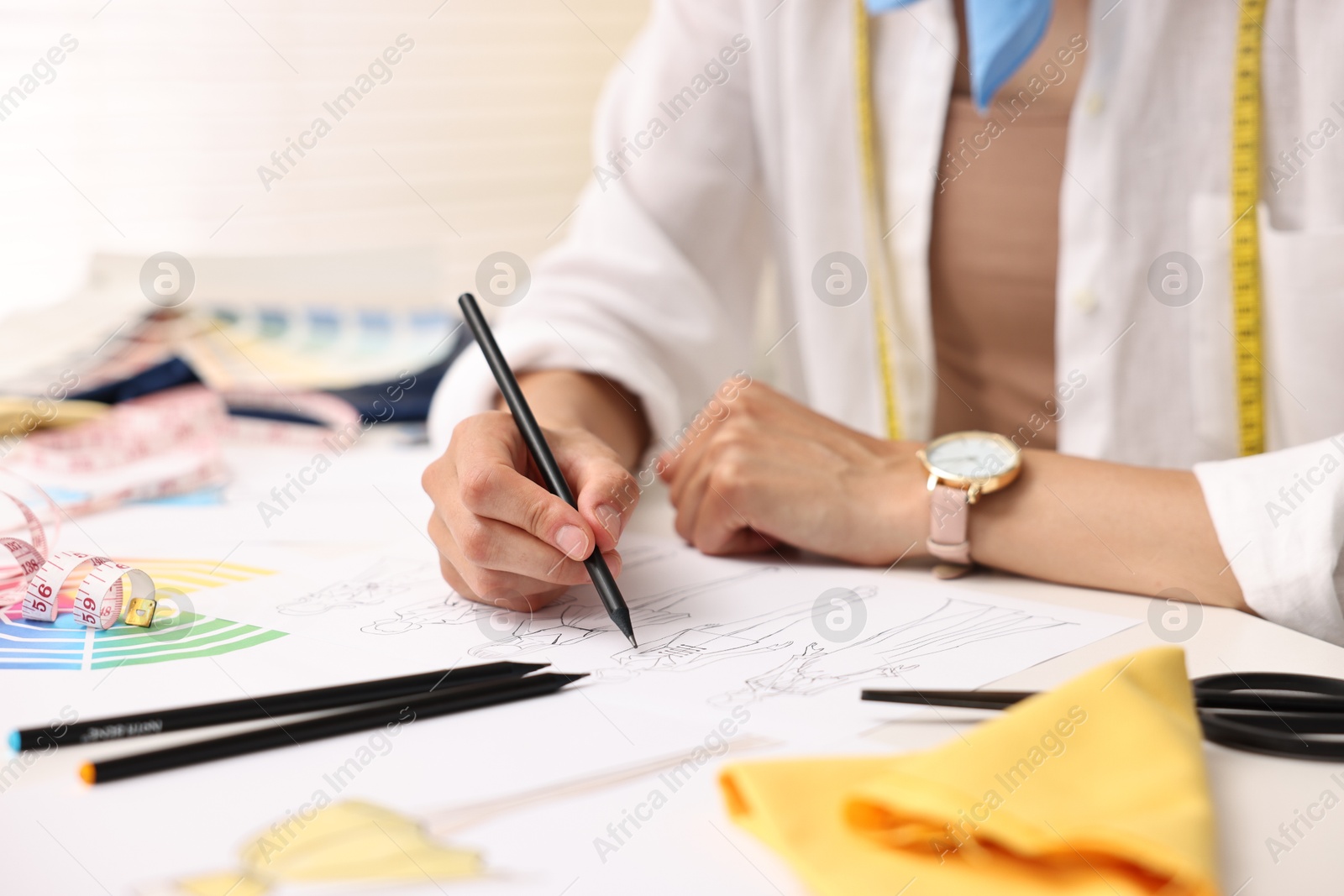 Photo of Fashion designer drawing sketch of beautiful outfit at table in workshop, closeup