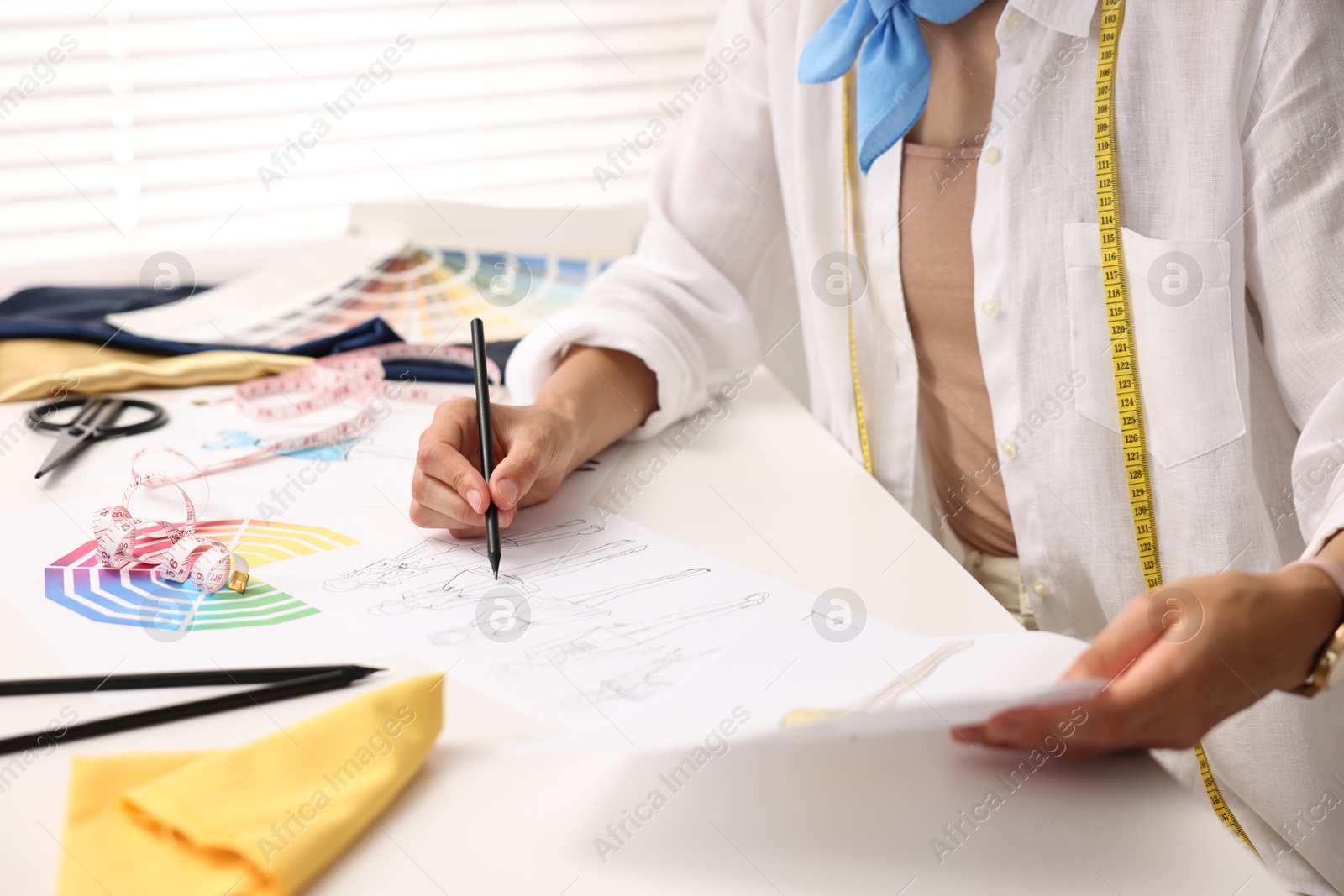 Photo of Fashion designer drawing sketch of beautiful outfit at table in workshop, closeup