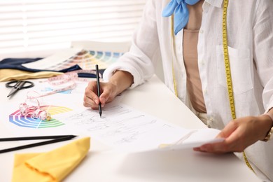 Photo of Fashion designer drawing sketch of beautiful outfit at table in workshop, closeup