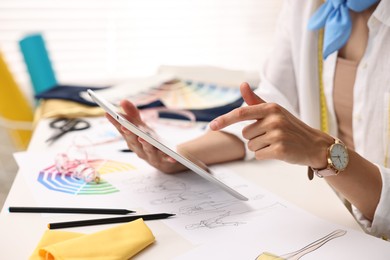 Fashion designer with tablet working at table in workshop, closeup