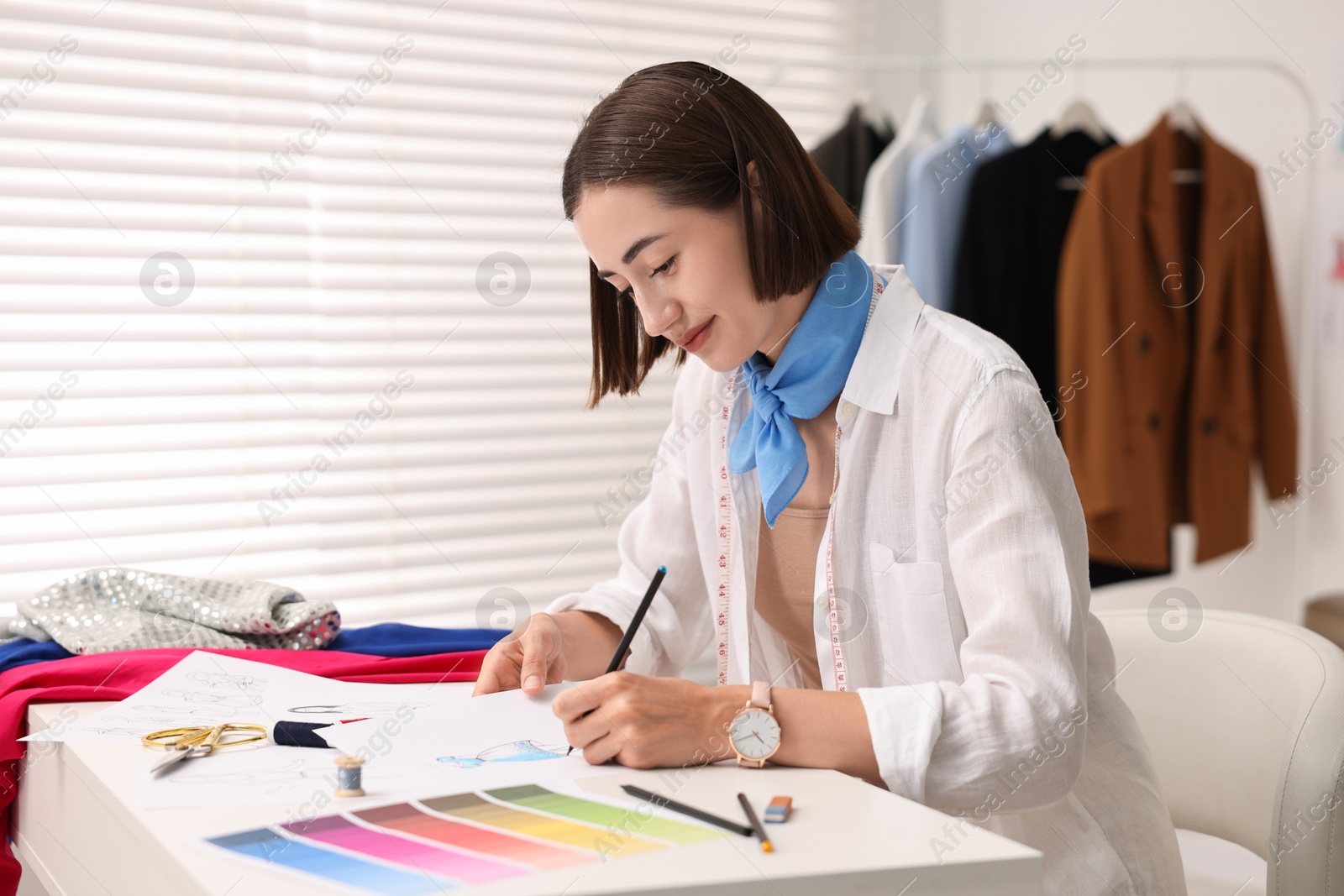 Photo of Fashion designer drawing sketch of dress at table in workshop