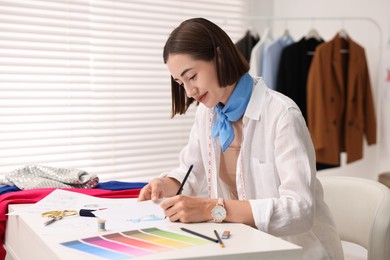 Photo of Fashion designer drawing sketch of dress at table in workshop