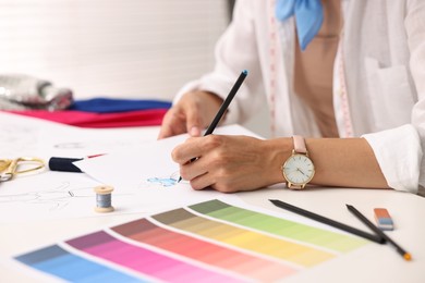 Photo of Fashion designer drawing sketch of dress at table in workshop, closeup