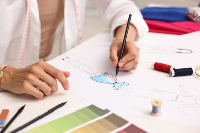 Photo of Fashion designer drawing sketch of dress at table in workshop, closeup