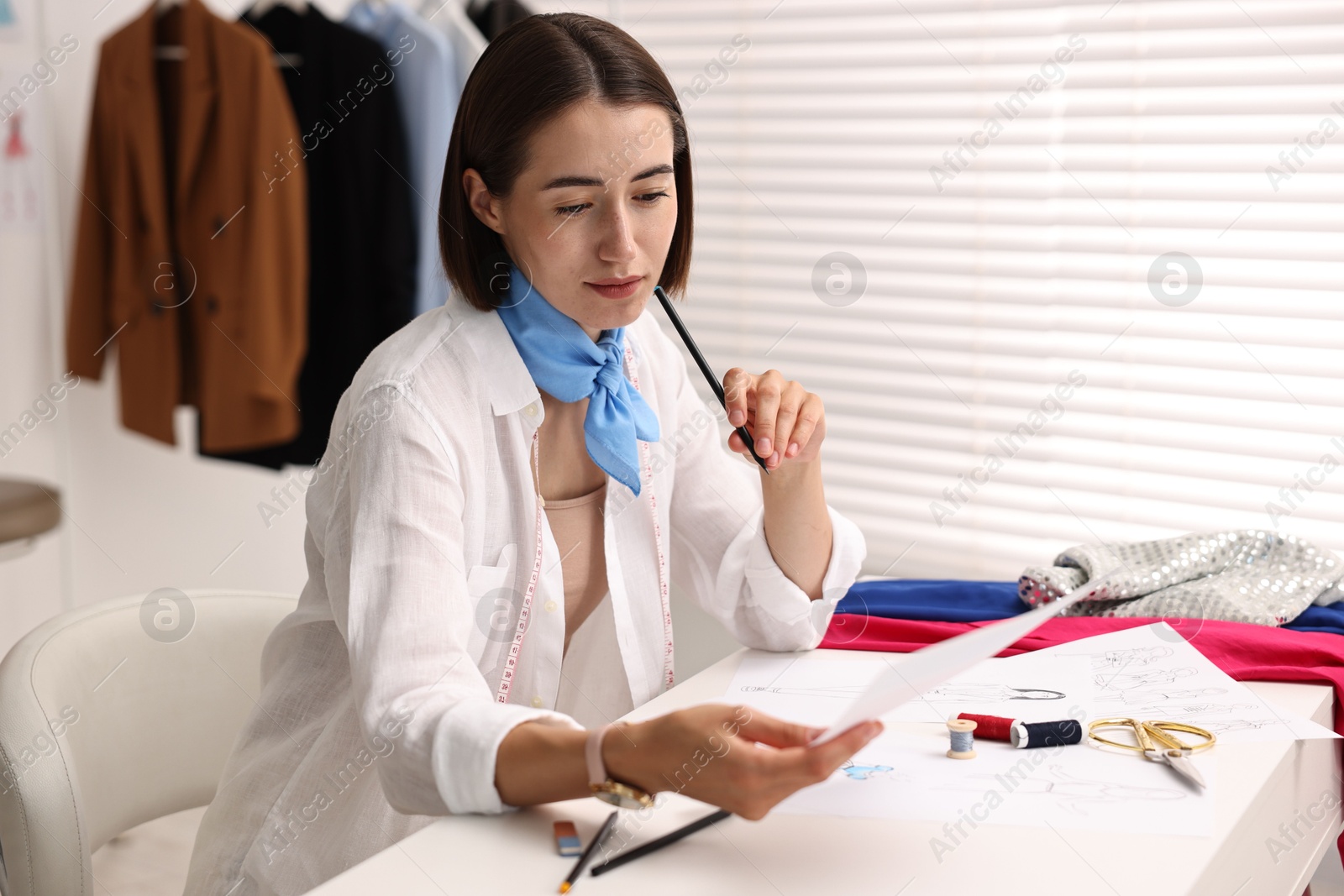 Photo of Fashion designer with pencil and sketch at table in workshop