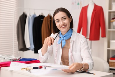 Photo of Fashion designer with pencil and sketch at table in workshop