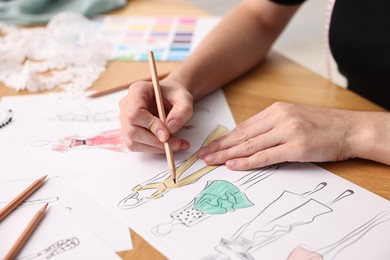 Fashion designer drawing sketch of beautiful dress at wooden table, closeup