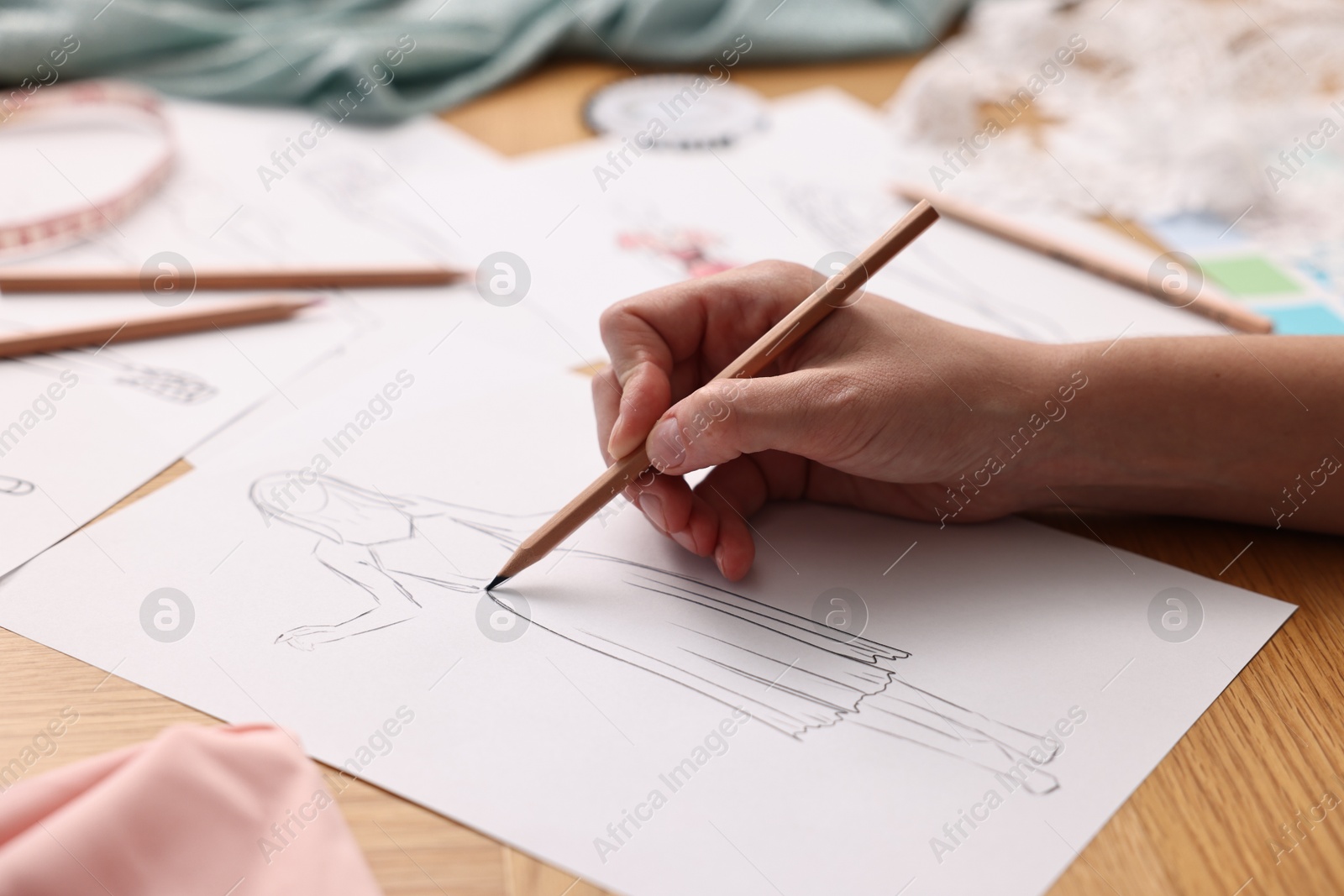 Photo of Fashion designer drawing sketch of dress at wooden table, closeup