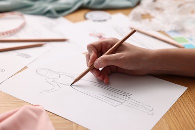 Fashion designer drawing sketch of dress at wooden table, closeup