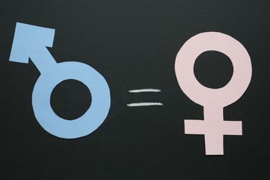 Photo of Equals sign between female and male gender symbols on chalkboard, flat lay