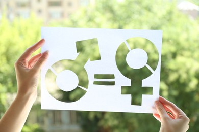 Photo of Gender equality concept. Woman holding paper with female and male symbols outdoors, closeup