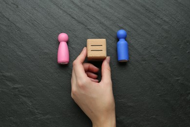 Photo of Gender equality concept. Woman holding wooden cube with equals sign between female and male figures at grey textured background, top view