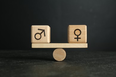 Photo of Wooden balance scales with cubes showing concept of equality between men and women against grey background