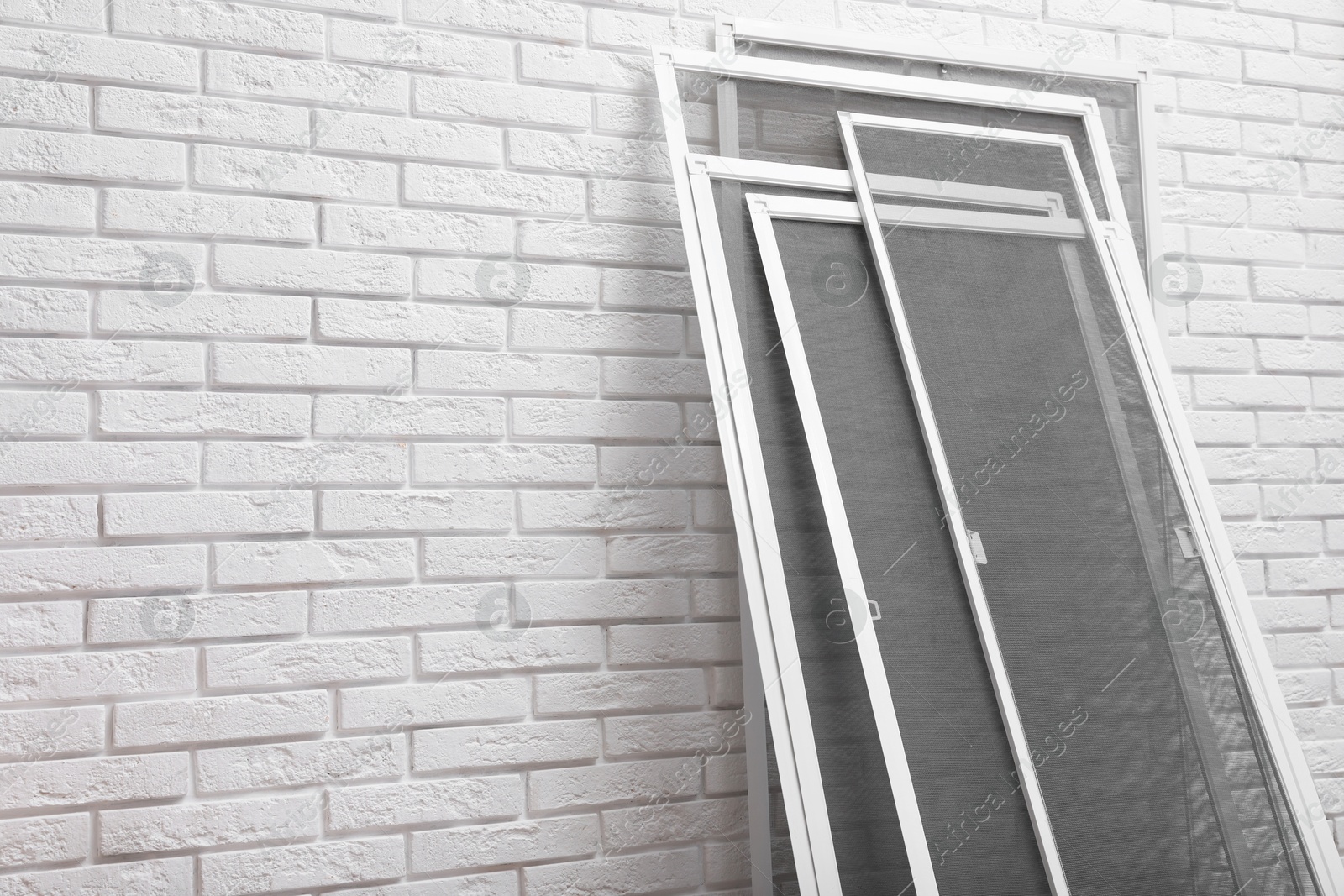 Photo of Set of window screens near white brick wall. Space for text