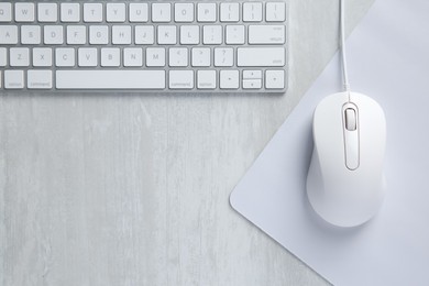 Photo of Wired mouse with mousepad and computer keyboard on light wooden table, flat lay. Space for text