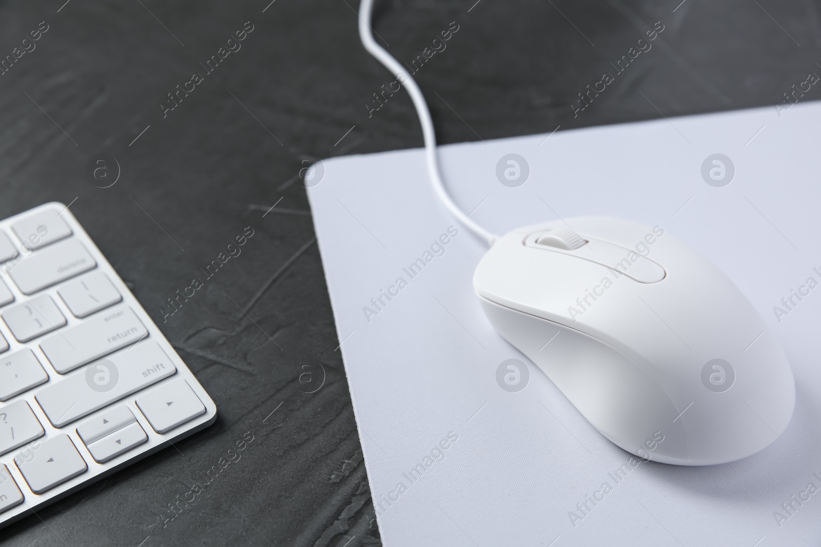 Photo of Wired mouse with mousepad and computer keyboard on dark textured table, closeup