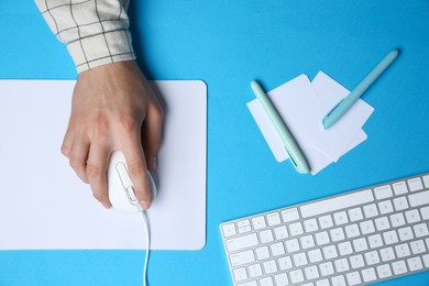 Photo of Man working with mouse, computer keyboard and stationery at light blue table, top view