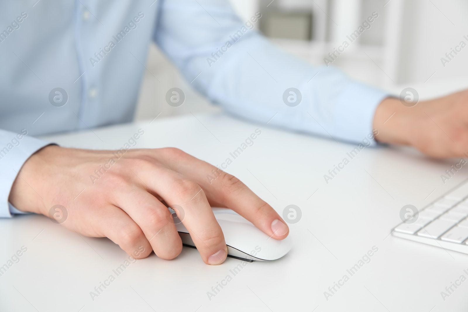 Photo of Man working with wireless mouse and computer keyboard at white table indoors, closeup