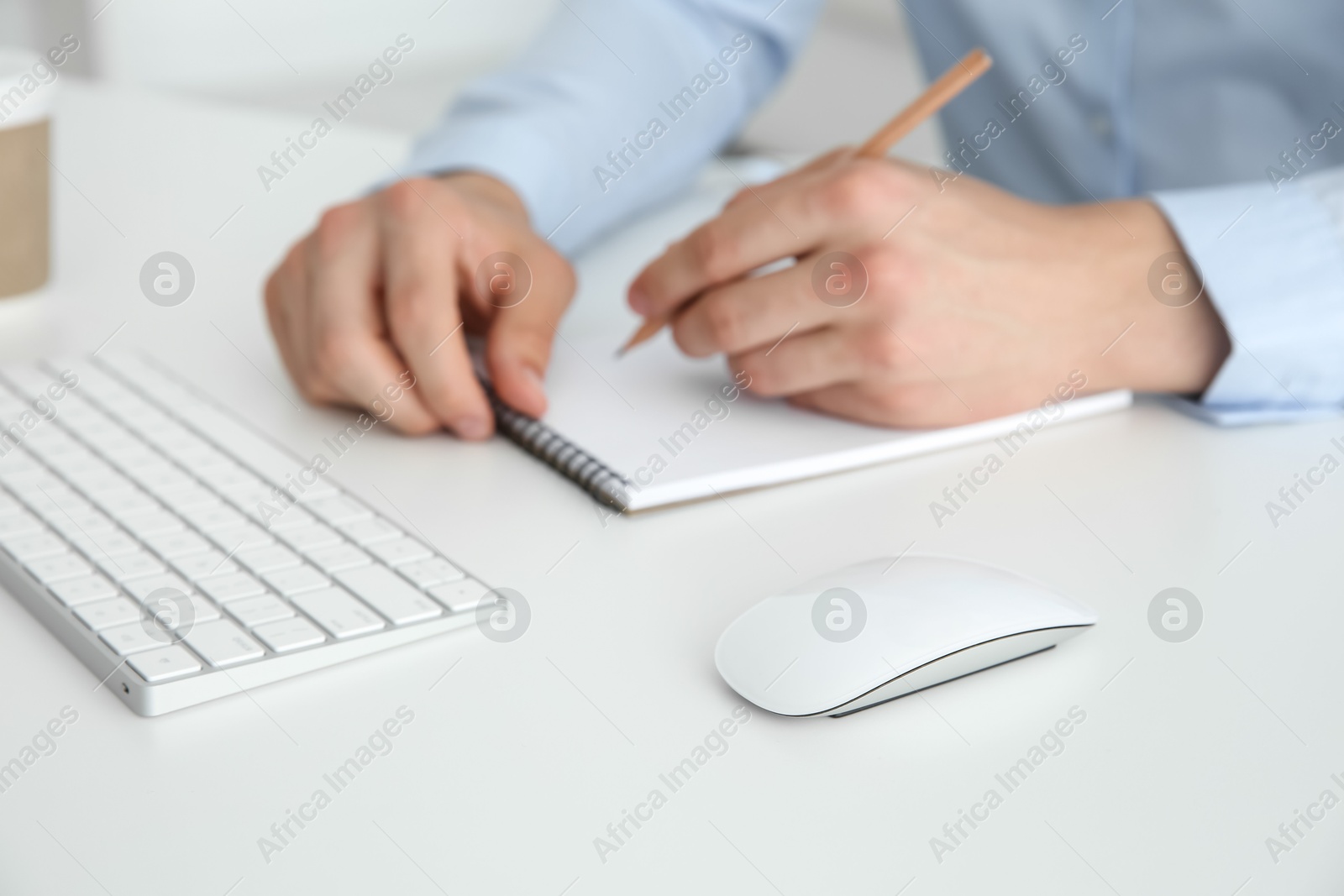 Photo of Wireless mouse on white table. Man writing in notebook indoors, selective focus